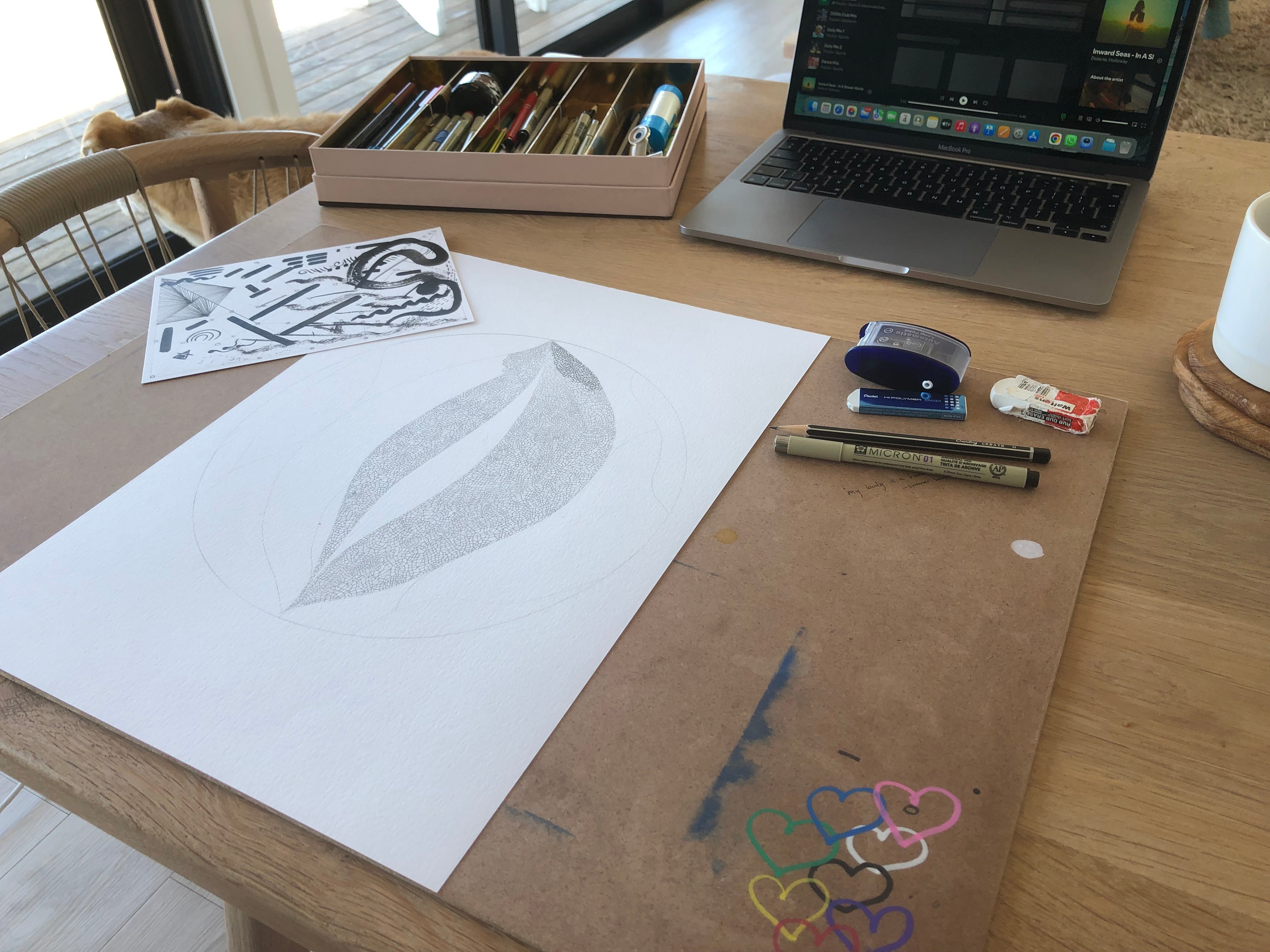 Home workspace with ink drawing in progress on dining table, art supplies nearby, laptop pushed aside showing transition from digital to analog work.